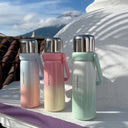 Three gradient-colored water bottles on a white surface with a scenic background